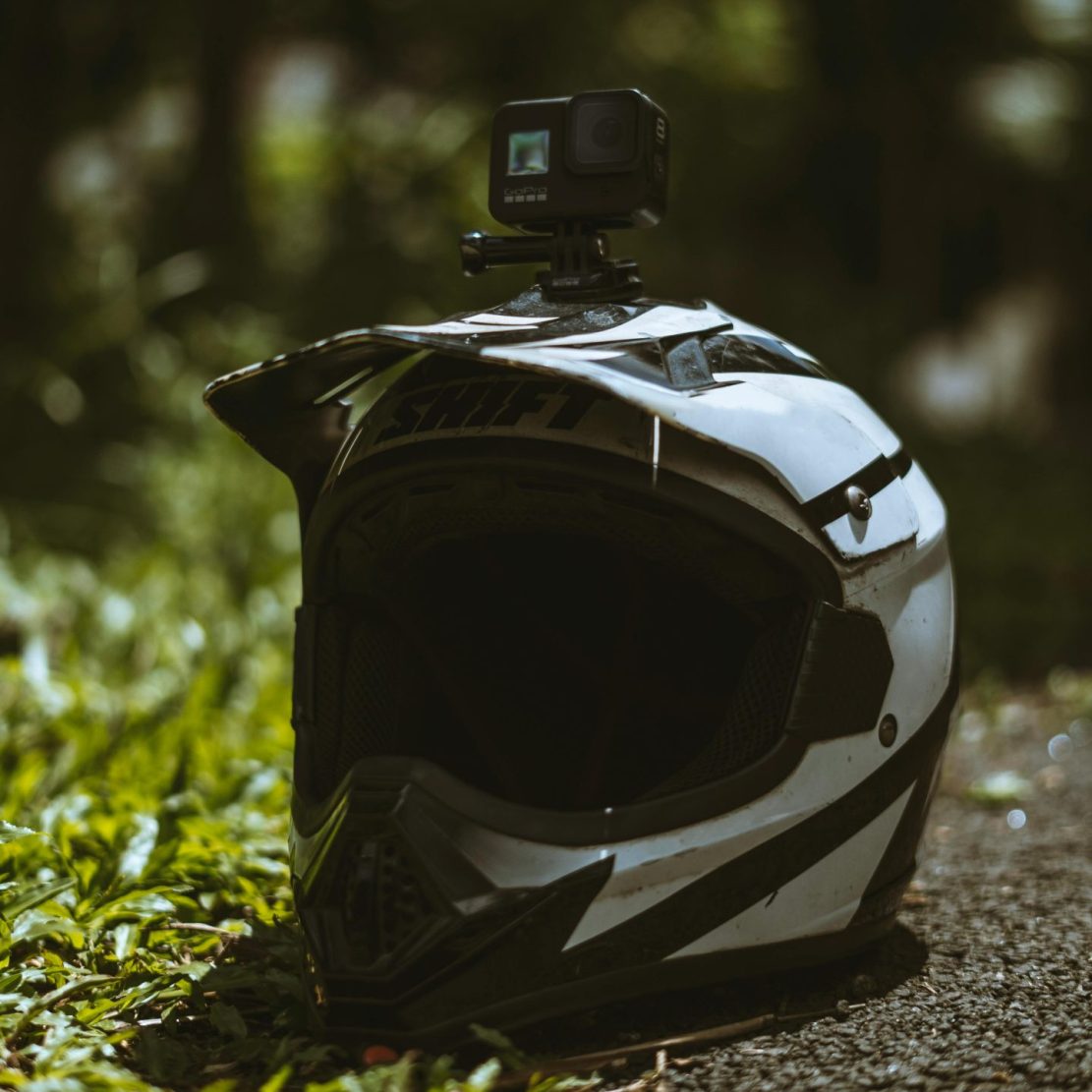 A close-up of a motorcycle helmet with an action camera on a forest pathway.